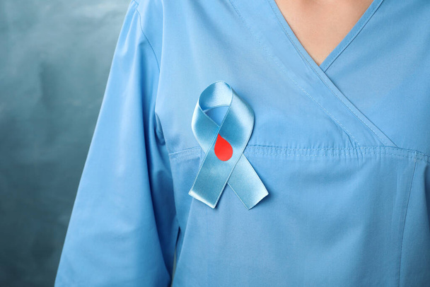 Doctor with light blue ribbon and paper blood drop on color background, closeup. World Diabetes Day - Photo, Image