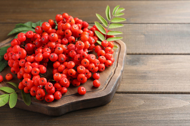 Board with fresh ripe rowan berries and leaves on wooden table. Space for text - Valokuva, kuva