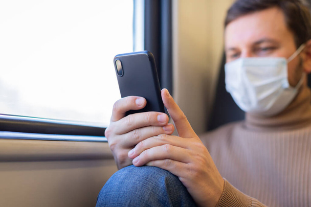 A man wearing a medical mask rides a train and uses his phone. - Valokuva, kuva