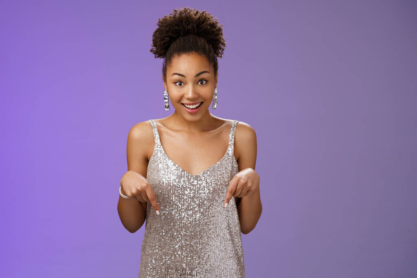 Excited surprised charming glamour african-american woman elegant silver glittering dress smiling wondered touched pointing down index fingers widen eyes astonished pleased awesome present - Photo, Image