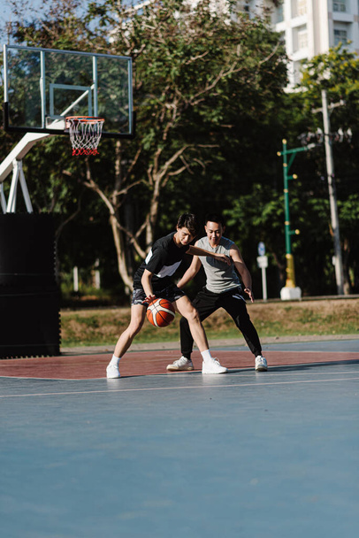 Αθλητισμός και ψυχαγωγία έννοια δύο άνδρες παίκτες μπάσκετ απολαμβάνοντας να παίζουν μπάσκετ μαζί στο γήπεδο του αθλητισμού. - Φωτογραφία, εικόνα