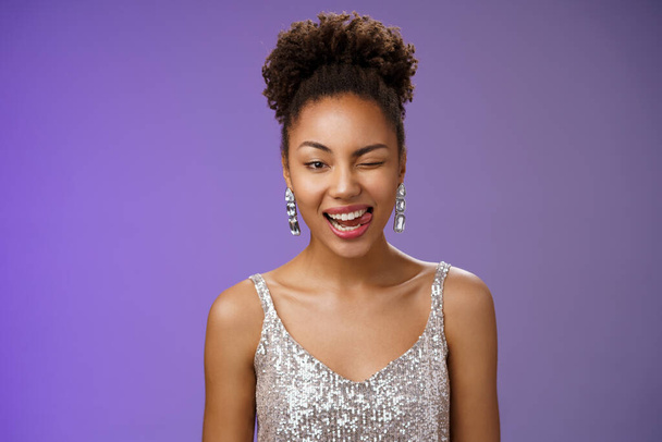 Close-up attractive african-american woman in silver trendy evening dress earrings winking happily show tongue sassy gladly enjoying awesome disco party dancing foolind around have fun - Photo, Image