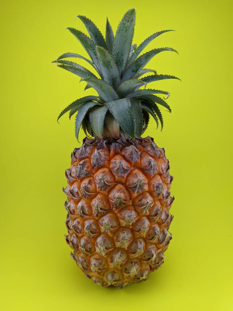 A vertical shot of a pineapple in a yellow background - Foto, afbeelding