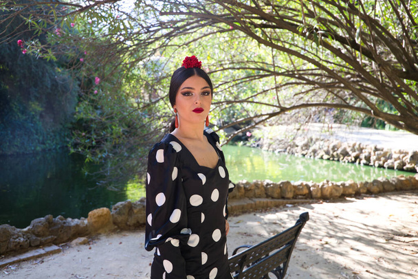 Испанский, красивый, брюнетка танцовщица фламенко с типичным платьем фламенко в черном с белыми точками польки. Она танцует в парке в Севилье. Концепция фламенко. - Фото, изображение