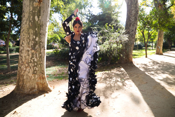 Espanjalainen, kaunis, brunette flamenco tanssija tyypillinen flamenco mekko musta valkoinen pilkkuja. Hän tanssii puistossa Sevillassa. Flamenco käsite ihmiskunnan kulttuuriperintö. - Valokuva, kuva