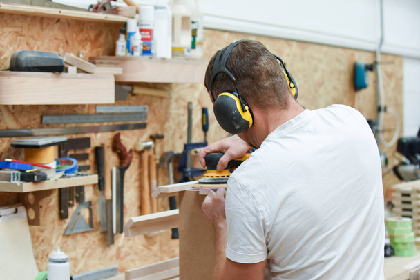 A man using a power tool electric sander to craft wood in the carpentry trade - Photo, Image