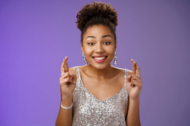 Весела оптимістична чарівна дівчина-афроамериканець, яка підтримує друга, хоче виграти перший приз, крокуючи пальцями, і посміхається в широкому одязі блискуча срібна сукня, очікуючи удачі. - Фото, зображення
