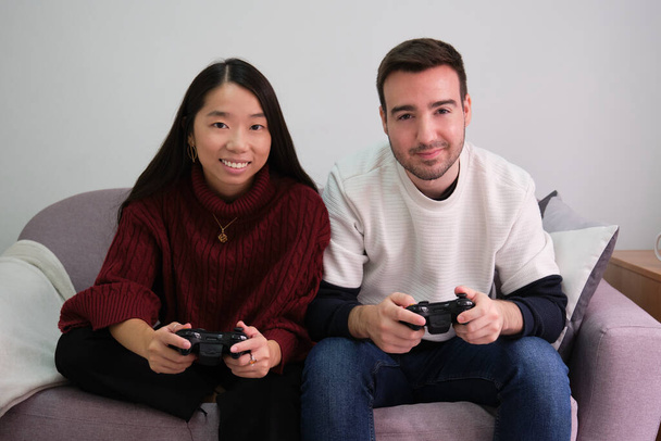 Jeune couple multiracial jouant à des jeux vidéo et utilisant des contrôleurs joystick. - Photo, image