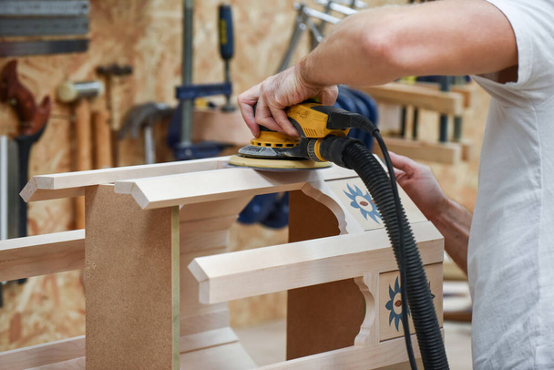 Um homem usando uma lixadeira elétrica ferramenta elétrica para artesanato de madeira no comércio de carpintaria - Foto, Imagem