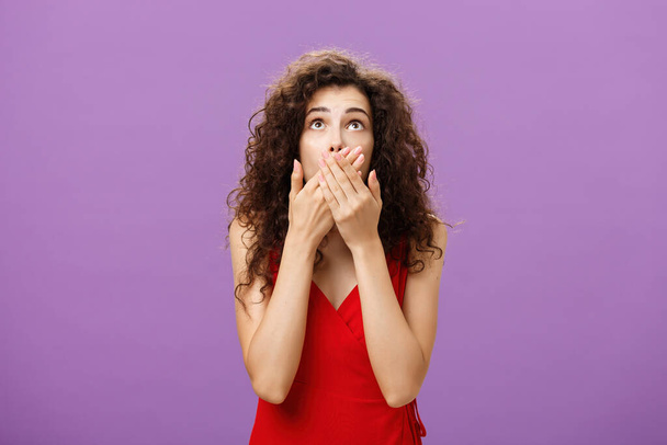 Woman being shocked and stunned seing guy about fall down from tree gasping feeling nervous covering opened from amazement mouth looking up standing intense over purple background in evening red dress - Photo, Image