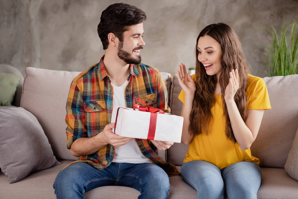 Photo of impressed beautiful young lovers dressed casual clothes giving present box smiling indoors loft apartment - Fotó, kép
