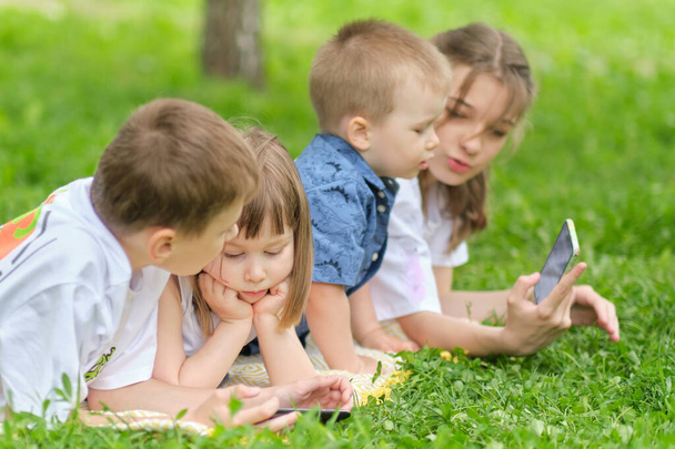 children friend group playing internet with mobile smartphone on grass. Happy children using smartphones sitting on the grass. Brothers and sister. - Foto, imagen