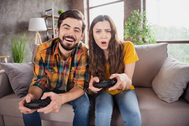 Photo of funny gamer couple hold gamepad play videogame enjoy weekend wear casual clothes sit couch home indoors - Photo, Image