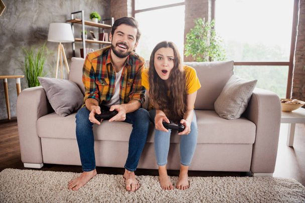 Photo of beautiful shocked young couple wear casual outfits sitting couch playing football playstation indoors house room - Foto, imagen