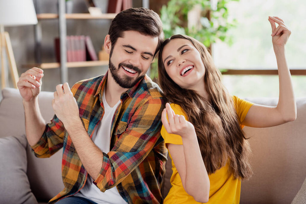 Photo of attractive funky young couple wear casual outfits sitting couch dancing smiling indoors house room - Фото, изображение