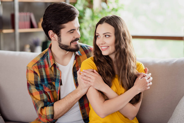 Photo of sweet tender young lovers dressed casual clothes sitting sofa smiling cuddling looking eyes indoors loft apartment - Φωτογραφία, εικόνα