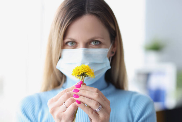 Woman in protective medical mask sniffing yellow flowers - Fotó, kép