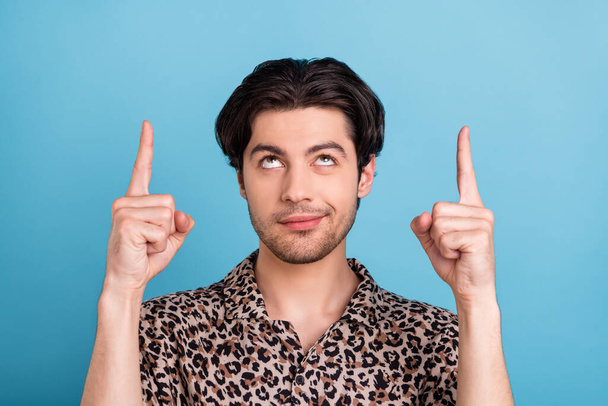 Portrait of attractive curious brunette guy pointing up copy blank space place isolated over vibrant blue color background - 写真・画像