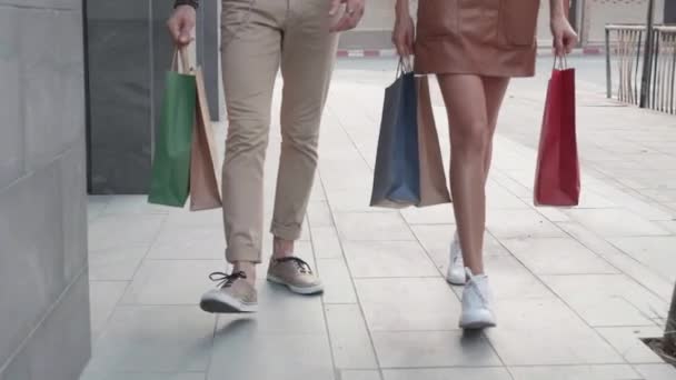 Closeup legs of two people young man and woman walking and holding shopping bag in the street, friends is shopaholic for purchase together, relationship of couple is consumerism with satisfied. - Footage, Video