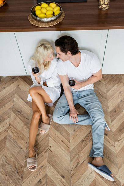 top view of young couple holding glasses of wine while sitting on kitchen floor - Fotoğraf, Görsel