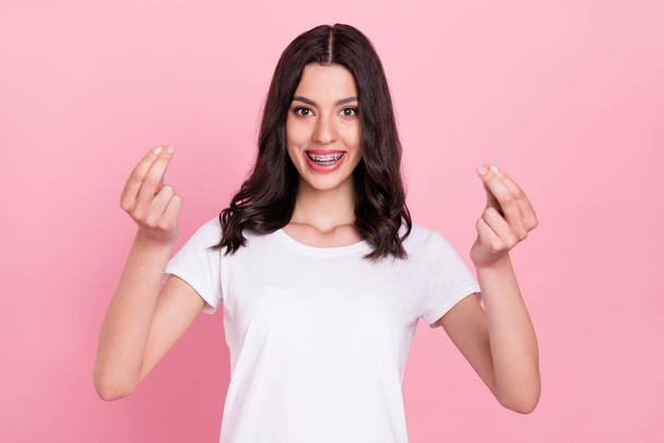 Photo of positive young happy cheerful woman make fingers money sign isolated on pastel pink color background - 写真・画像