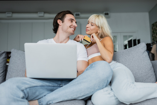 ευτυχισμένο ζευγάρι με πιστωτική κάρτα και φορητό υπολογιστή κοιτάζοντας ο ένας τον άλλο κάνει online ψώνια  - Φωτογραφία, εικόνα