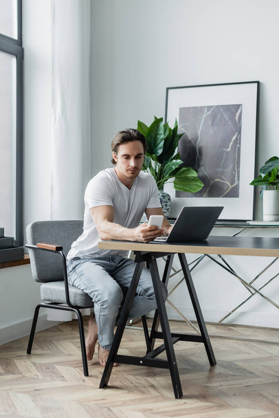 young man using smartphone near laptop on desk - Fotoğraf, Görsel