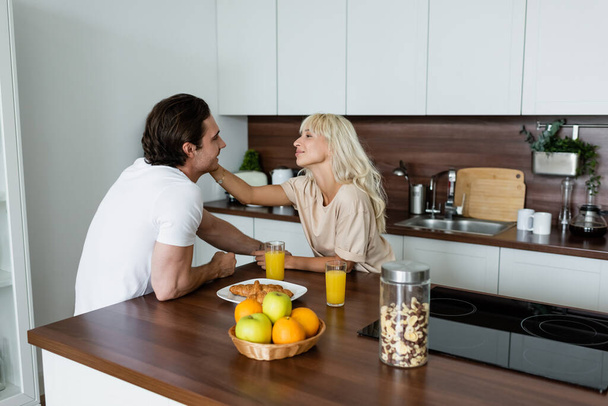 happy woman touching face of smiling boyfriend in kitchen  - Foto, Imagen