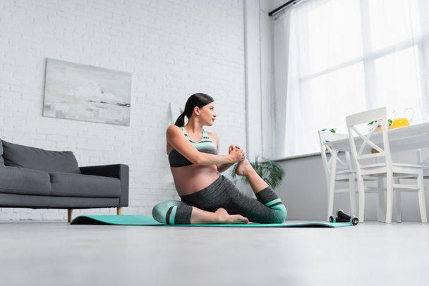 surface level view of young pregnant woman stretching in yoga pose at home - Photo, Image