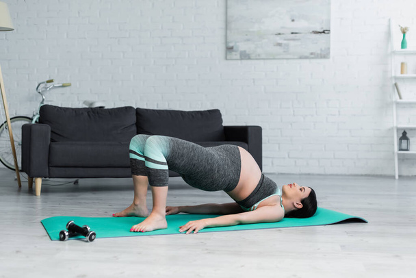 Schwangere in Sportbekleidung übt Bridge-Pose auf Yogamatte  - Foto, Bild