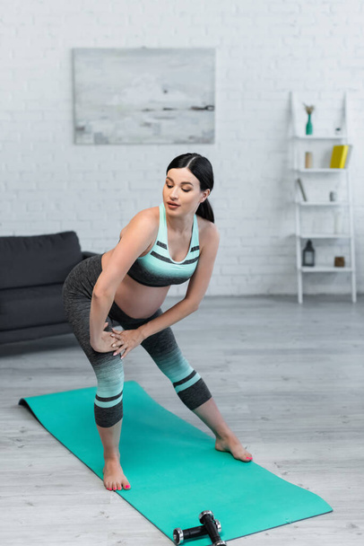 young pregnant woman warming up on fitness mat at home - Valokuva, kuva