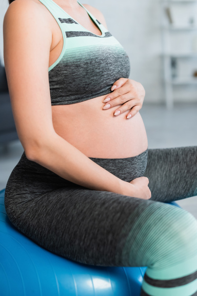 cropped view of pregnant woman in sportswear touching belly while exercising on fitness ball - Фото, зображення