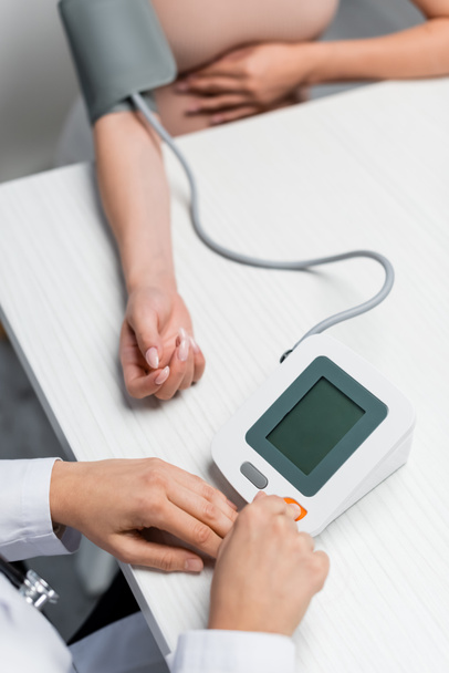 vista parcial del médico que mide la presión arterial de la mujer embarazada sobre fondo borroso - Foto, Imagen