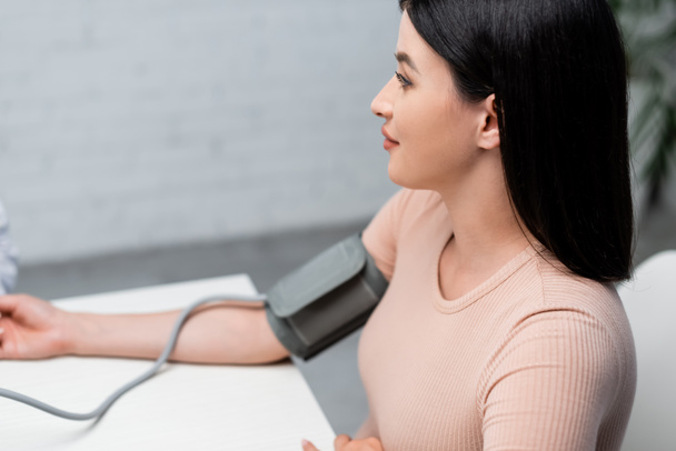 brunette vrouw meten van bloeddruk met tonometer in kliniek - Foto, afbeelding
