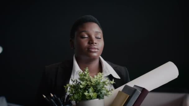 Kirúgott fekete női alkalmazott elhagyja az irodát egy doboz személyes cuccal. - Felvétel, videó