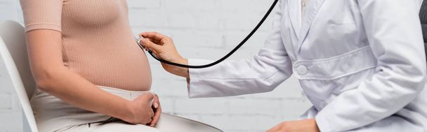 részleges nézet az orvos vizsgálja hasát terhes nő sztetoszkóppal, banner - Fotó, kép
