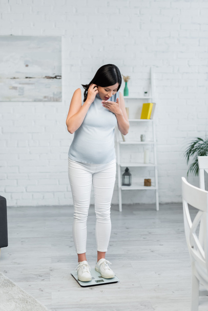 mujer embarazada asombrada estimar el peso corporal en básculas de piso en casa - Foto, imagen