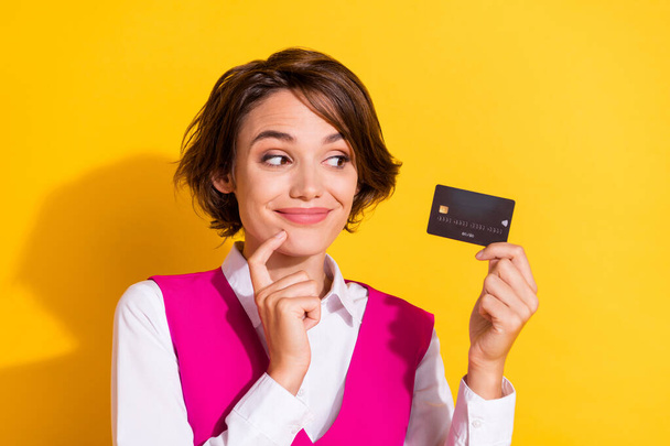 Photo of sweet tricky young lady wear pink suit holding looking bank card finger chin isolated yellow color background - Фото, зображення