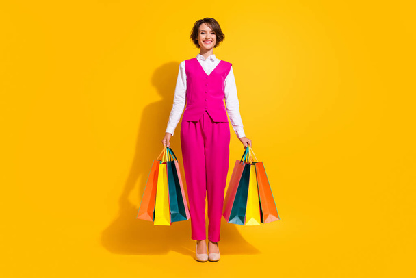 Photo of pretty charming young lady wear pink suit holding bargains smiling isolated yellow color background - Fotó, kép