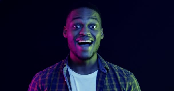 Nahaufnahme Porträt von emotionalen afrikanisch-amerikanischen Kerl berührt Wangen in Erstaunen, Neonlicht - Filmmaterial, Video