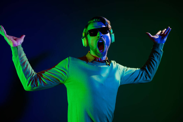 Photo of funky young cheerful man wear sunglass headset good mood sing clubber isolated on neon background - Фото, зображення