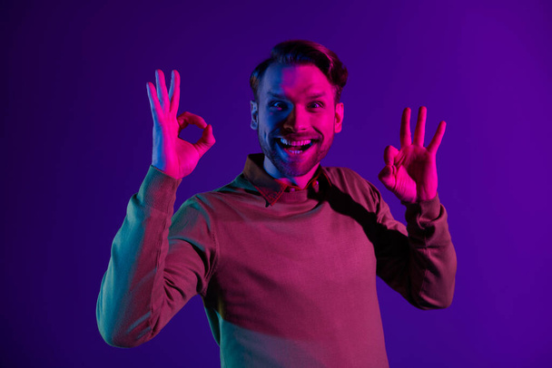 Photo of young cheerful man happy positive smile show okay sign cool ads advice alright isolated over neon color background - Photo, Image