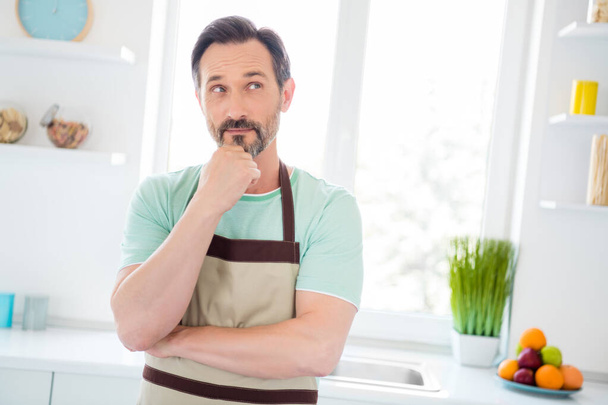 Fotografie legrační přemýšlivý věk muž oblečený modrý t-shirt zástěra vaření usmívá vnitřní domácí pokoj - Fotografie, Obrázek