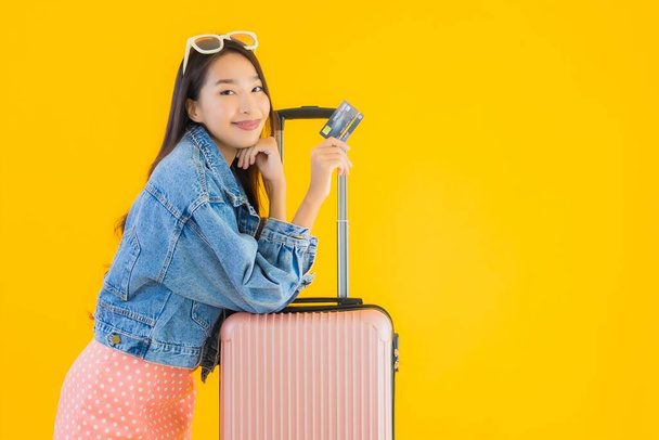 Retrato hermosa joven asiática mujer con equipaje bolsa de viaje con pasaporte y billete de embarque en amarillo aislado fondo
 - Foto, imagen