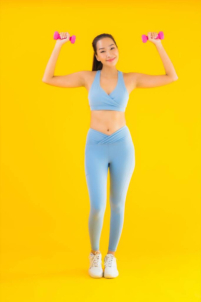 Ritratto bella giovane donna asiatica con manubri e abbigliamento sportivo pronti per l'esercizio su sfondo giallo isolato - Foto, immagini