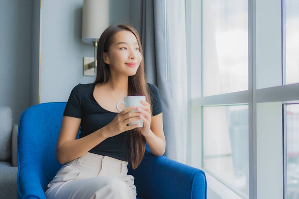 Ritratto bella giovane donna asiatica tenere la tazza di caffè sul divano sedia nella zona soggiorno - Foto, immagini