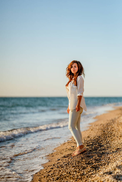  Urocza młoda kobieta w białej koszuli i dżinsach na spokojnej, romantycznej plaży nad morzem. Koncepcja wakacji letniej kobiety. Koncepcja aktywnego życia. - Zdjęcie, obraz