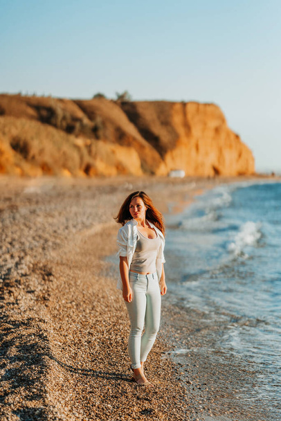  Urocza młoda kobieta w białej koszuli i dżinsach na spokojnej, romantycznej plaży nad morzem. Koncepcja wakacji letniej kobiety. Koncepcja aktywnego życia. - Zdjęcie, obraz