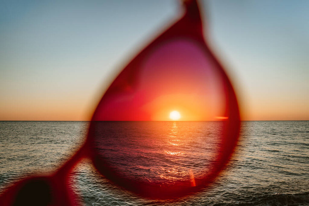 Όμορφο ηλιοβασίλεμα πλαισιωμένο από κόκκινα γυαλιά ηλίου σε σχήμα καρδιάς. Η έννοια των ευτυχισμένων καλοκαιρινών θαλασσίων διακοπών - Φωτογραφία, εικόνα