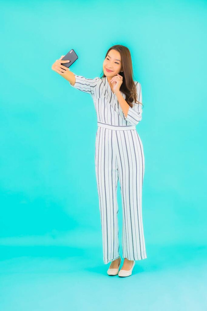 Retrato hermosa joven asiática mujer uso inteligente teléfono móvil sobre fondo azul - Foto, Imagen